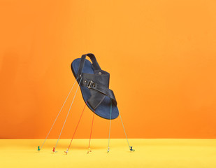 flying leather man's sandal, held by threads on a yellow-orange background.