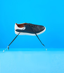 flying leather men's black sneaker with a white sole held by threads on a blue background.