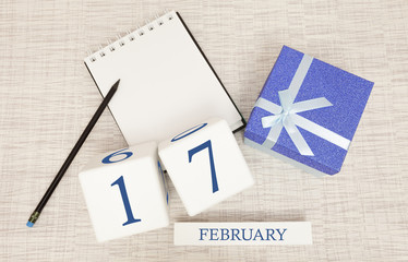 Calendar with trendy blue text and numbers for February 17 and a gift in a box.