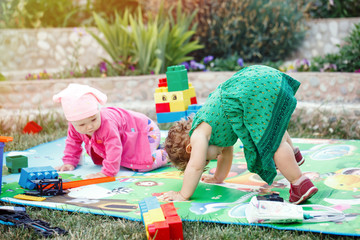 Two children baby girls are sitting on green meadow playing and smile