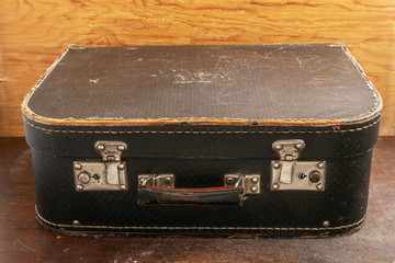 Old suitcase with a shabby handle and rusty locks on a wooden background.