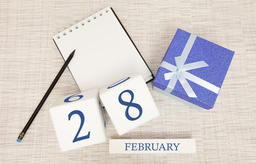Calendar with trendy blue text and numbers for February 28 and a gift in a box.