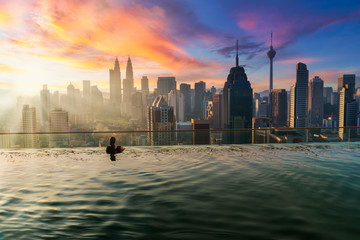 Asian businesswoman relax in swimming pool on roof top behind beautiful city view kuala lumpur in sunrise sky morning, Malaysia