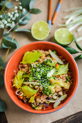 Bowl of stir fried udon noodles garnished with black sesame seeds and fresh mint with green chopsticks
