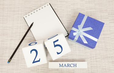 Calendar with trendy blue text and numbers for March 25 and a gift in a box.