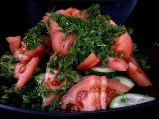Vegetable salad of cucumbers, tomatoes and herbs on a black background. Finely chopped vegetables in a salad bowl, close-up. Concept: healthy diet, fresh vegetables, vitamins.