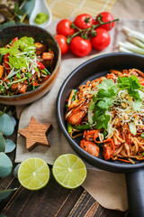 Bowl of stir fried udon noodles garnished with black sesame seeds and fresh mint with green chopsticks