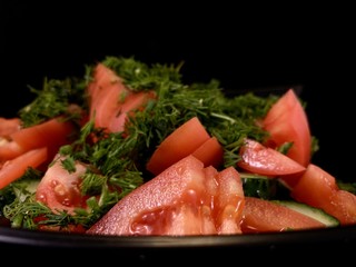 Vegetable salad of cucumbers, tomatoes and herbs on a black background. Finely chopped vegetables in a salad bowl, close-up. Concept: healthy diet, fresh vegetables, vitamins.