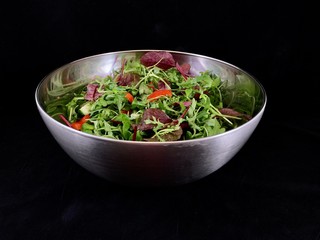 Vegetable salad of cucumbers, tomatoes and herbs on a black background. Finely chopped vegetables in a salad bowl, close-up. Concept: healthy diet, fresh vegetables, vitamins.