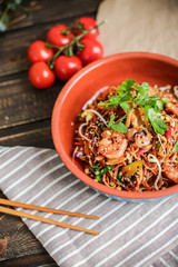 Bowl of stir fried udon noodles garnished with black sesame seeds and fresh mint with green chopsticks