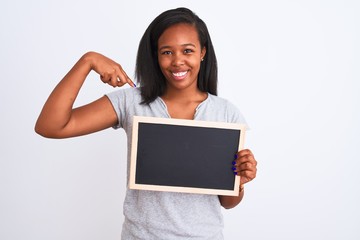 Young african american woman holding blank school blackboard over isolated background with surprise face pointing finger to himself