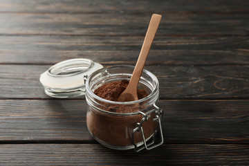 Glass jar with cocoa powder and spoon on wooden background, close up
