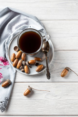 Hot coffee made from acorns in a glass with a napkin is a tonic drink with a coffee flavor, rich color and pleasant aroma. On a white wooden background