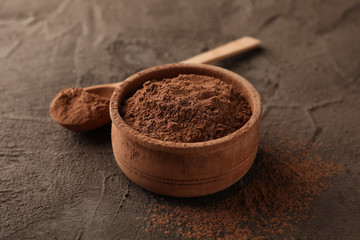 Bowl with cocoa powder and spoon on brown background, closeup