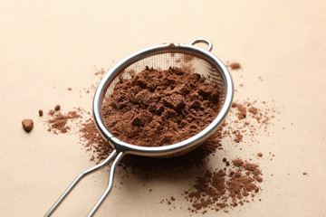Strainer with cocoa powder on cardboard background, close up