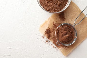 Glass bowl and strainer with cocoa powder, baking paper on white background, copy space