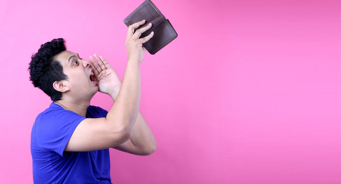 A close-up portrait of a shocked, surprised speechless man asia, holding an empty wallet on pink  background in studio With copy space.