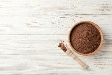 Wooden bowl and scoop with cocoa powder on white wood background, space for text