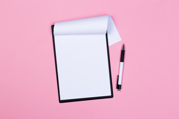 Clipboard with white sheet and pen on a pastel pink background. View from above. space for text