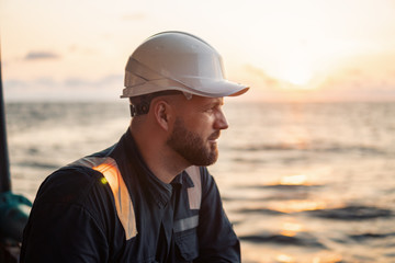 Marine Deck Officer or Chief mate on deck of offshore vessel or ship , wearing PPE personal protective equipment - helmet, coverall. He holds VHF walkie-talkie radio in hands.