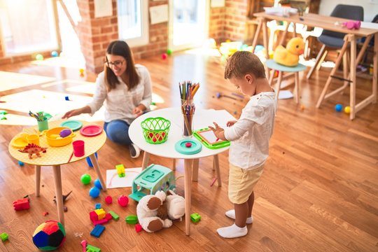 Beautiful teacher and toddler drawing using digital board around lots of toys at kindergarten