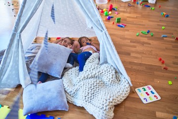 Adorable toddlers lying down over blanket inside tipi smiling at kindergarten