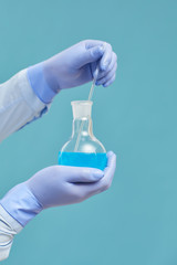 Close-up of chemist in protective gloves holding flask with blue liquid against the blue background