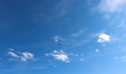 A plane flying against a blue sky with cirrus and cumulus clouds. The concept of travel, vacation, adventure.