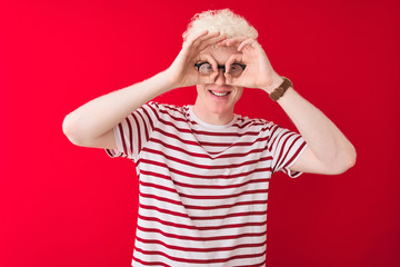 Young albino blond man wearing striped t-shirt and glasses over isolated red background doing ok...
