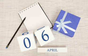 Calendar with trendy blue text and numbers for April 6 and a gift in a box.