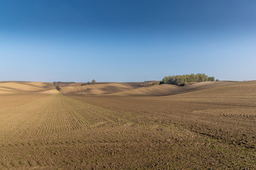 View of plowed land after the season in the Moravian Tuscany region's landscape full of ripples overlooking the village in the background during an afternoon sunny day without clouds