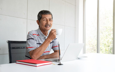 Fototapeta premium Senior Asian man using laptop computer in modern home office, businessman planning via internet concept, he relax and drinking coffee