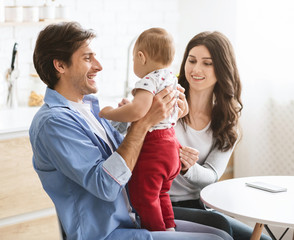 Proud father holding his baby son with love at kitchen