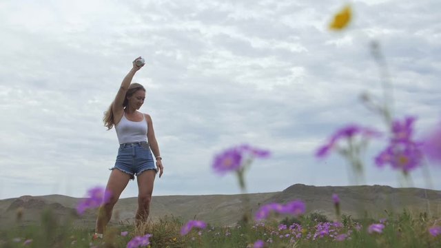 Camera follow hipster young woman in white t-shirt short jeans fluttering long hair. One girl dancing on field of grass portable music speaker smartphone. Happy drunk from life, youth and happiness.