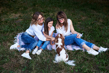 Two young blond women and one brunette girl, wearing jeans and white t-shirts, sitting on green...