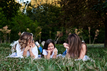 Two young blond women and one brunette girl, wearing white t-shirts, lying on mexican blanket on...