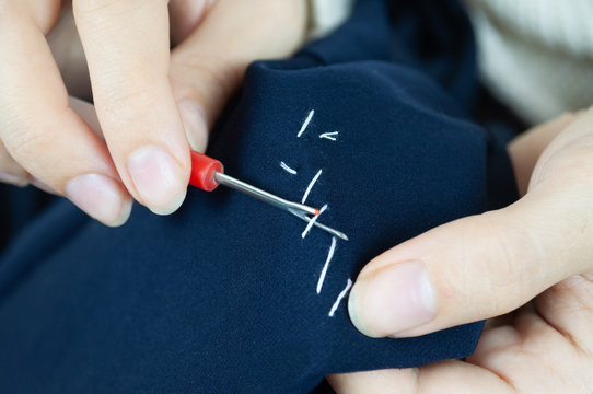 Woman's hads with seam ripper ripping stitches on fabric. Hands sewing, repairing clothes. Tailoring, homecraft concept
