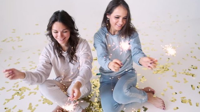 young brunettes with sparklers. Christmas mood..Attractive girls in pajamas with sparklers waiting for the holidays on a white background