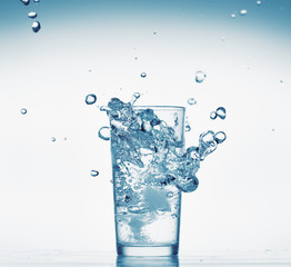 one glass of water with splash from falling ice cube, white background, isolated object