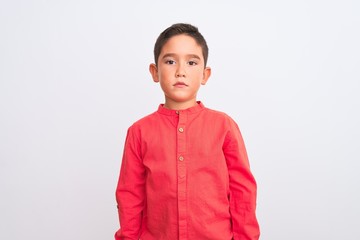 Beautiful kid boy wearing elegant red shirt standing over isolated white background Relaxed with serious expression on face. Simple and natural looking at the camera.