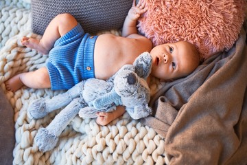 Adorable baby lying down on the sofa over blanket at home. Newborn relaxing and resting comfortable with doll