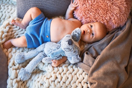 Adorable baby lying down on the sofa over blanket at home. Newborn relaxing and resting comfortable with doll