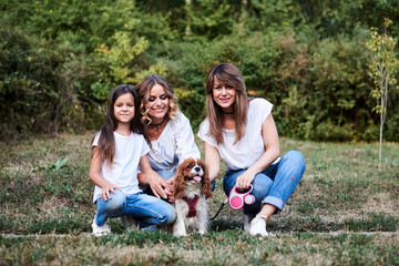 Two young blond women and one brunette girl, wearing casual clothes, kneeling on green grass in...