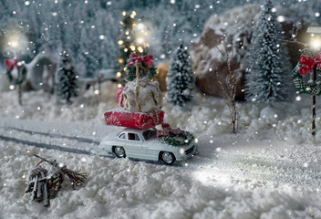Miniature classic car carrying a christmas gifts on snowy winter landscape