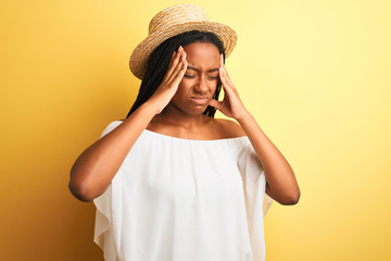 Young african american woman wearing white t-shirt and hat over isolated yellow background suffering from headache desperate and stressed because pain and migraine. Hands on head.