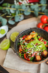 Bowl of stir fried udon noodles garnished with black sesame seeds and fresh mint with green chopsticks