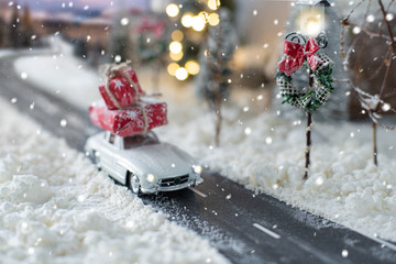 Miniature classic car carrying a christmas gifts on snowy winter landscape
