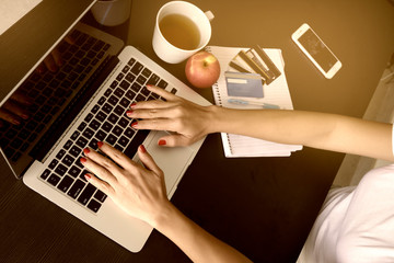 Woman hands on taptop keyboard typing with tea cup apple credit cards notebook pen and smartphone on wooden table background.