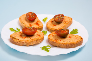 Tostadas con hummus y tomates cherry en un plato con perejil sobre fondo azul celeste.