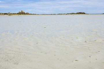 Ebb at a beach at the coastline of Brittany, blue sky with clouds